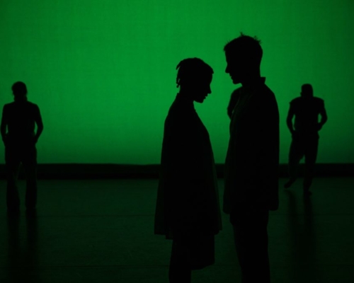 Four dancers - Kellie Ann Lynch, Myssi Robinson, Doug Gillespie, Jared Brown - silhouetted in green light stand in the frame. Two dancers, one furthest left and the other furthest right face the audience with heads tilted down. Two dancers in the center frame stand close together, facing each other in an inward moment.