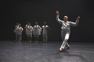 David Dorfman is in the foreground in motion. Six dancers stand in the background. Photo by Maria Baranova.
