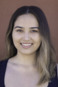 Artist Services' Erin Kenna is a half-Japanese woman with brown hair and blonde highlights. She has a gold nose ring and is smiling in front of a burnt orange background.