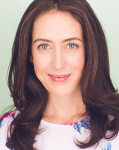 picture of Erin Roy highlighting the face of a middle aged white woman with dark brown hair wearing a floral print blouse and smiling in front of a light green background